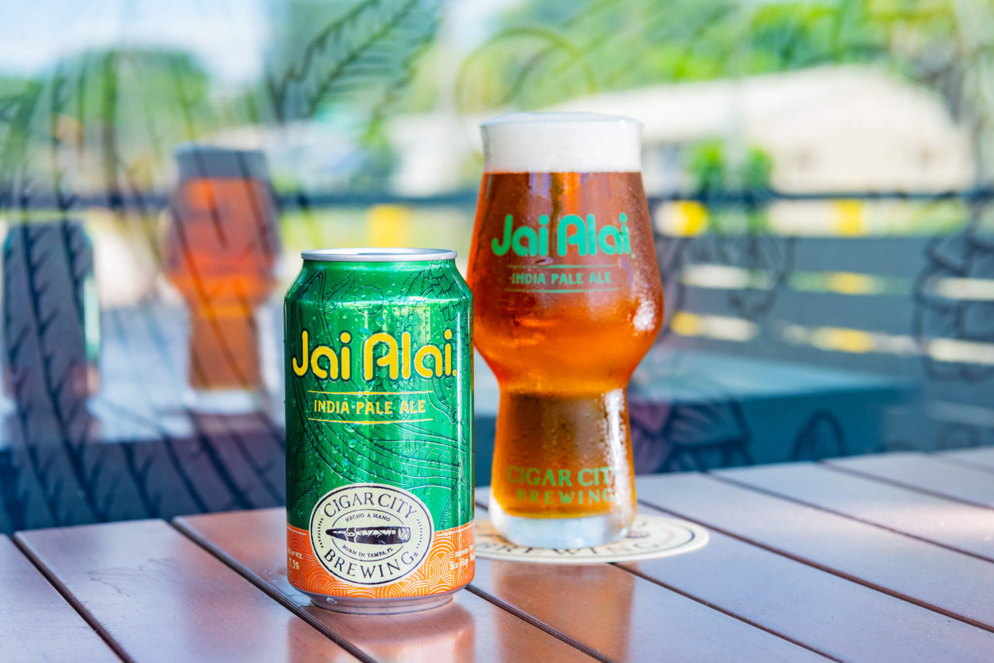 A can of Jai Alai IPA next to a draft pour of Jai Alai IPA in a glass with the Jai Alai IPA logo on it.